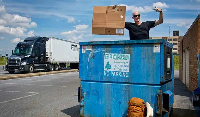 Fyr i en container holder et stykke pap til sit blaffeskilt med en lastbil forbi