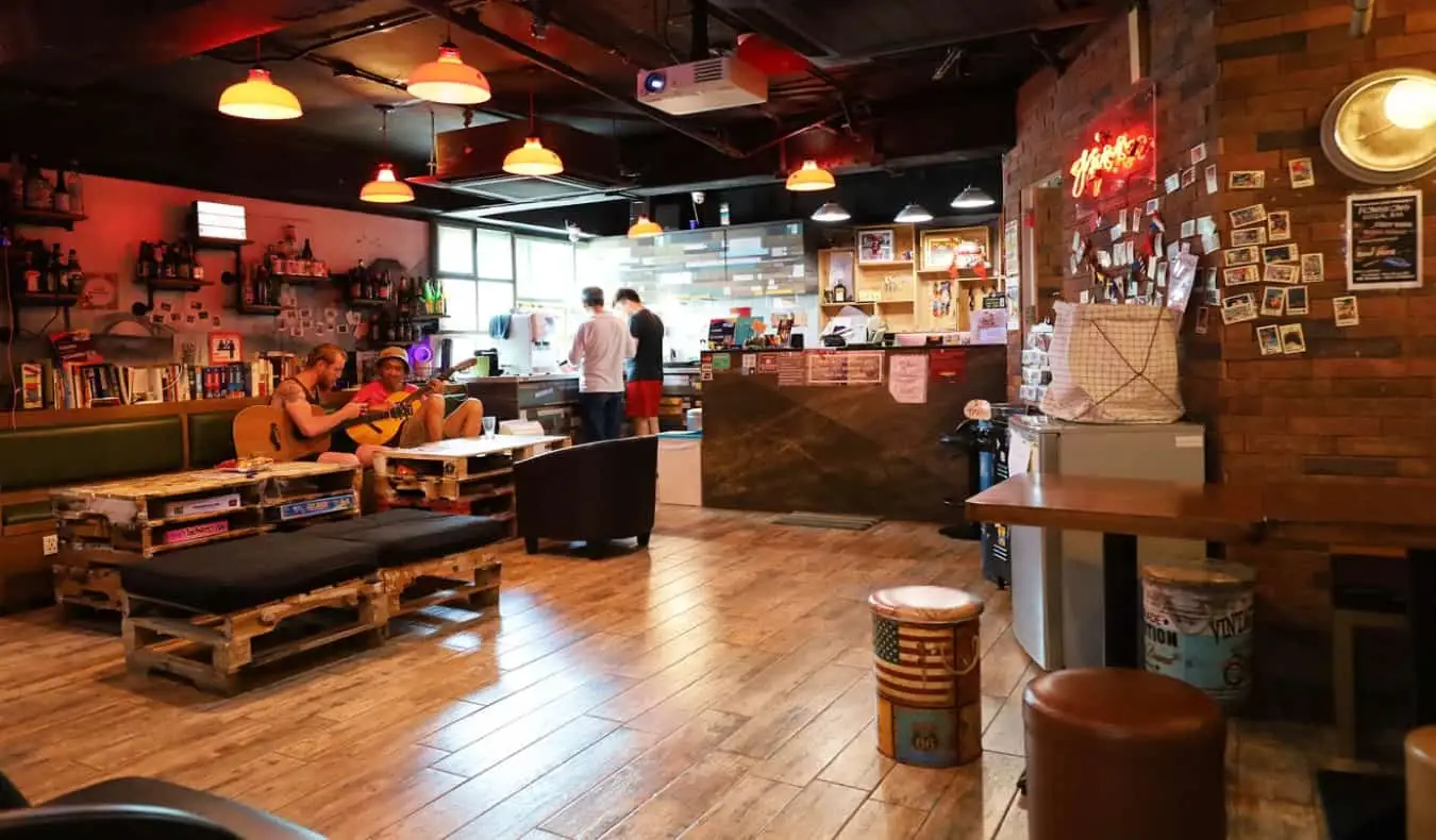 Sala comune accogliente, tutta in legno, con persone che suonano la chitarra allo Yesinn Hostel di Hong Kong