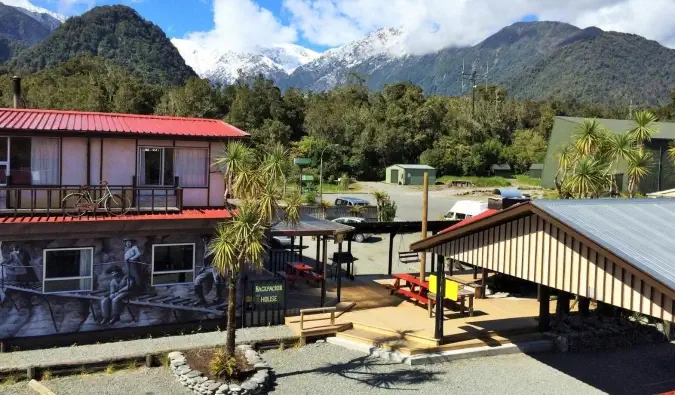 Buitenkant van de budgetaccommodatie Chateau Backpacker & Motels met bos op de achtergrond, in Franz Josef, Nieuw-Zeeland