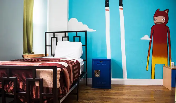 Tempat tidur single di kamar dengan mural yang dilukis di dinding di NY Moore Hostel di NYC.