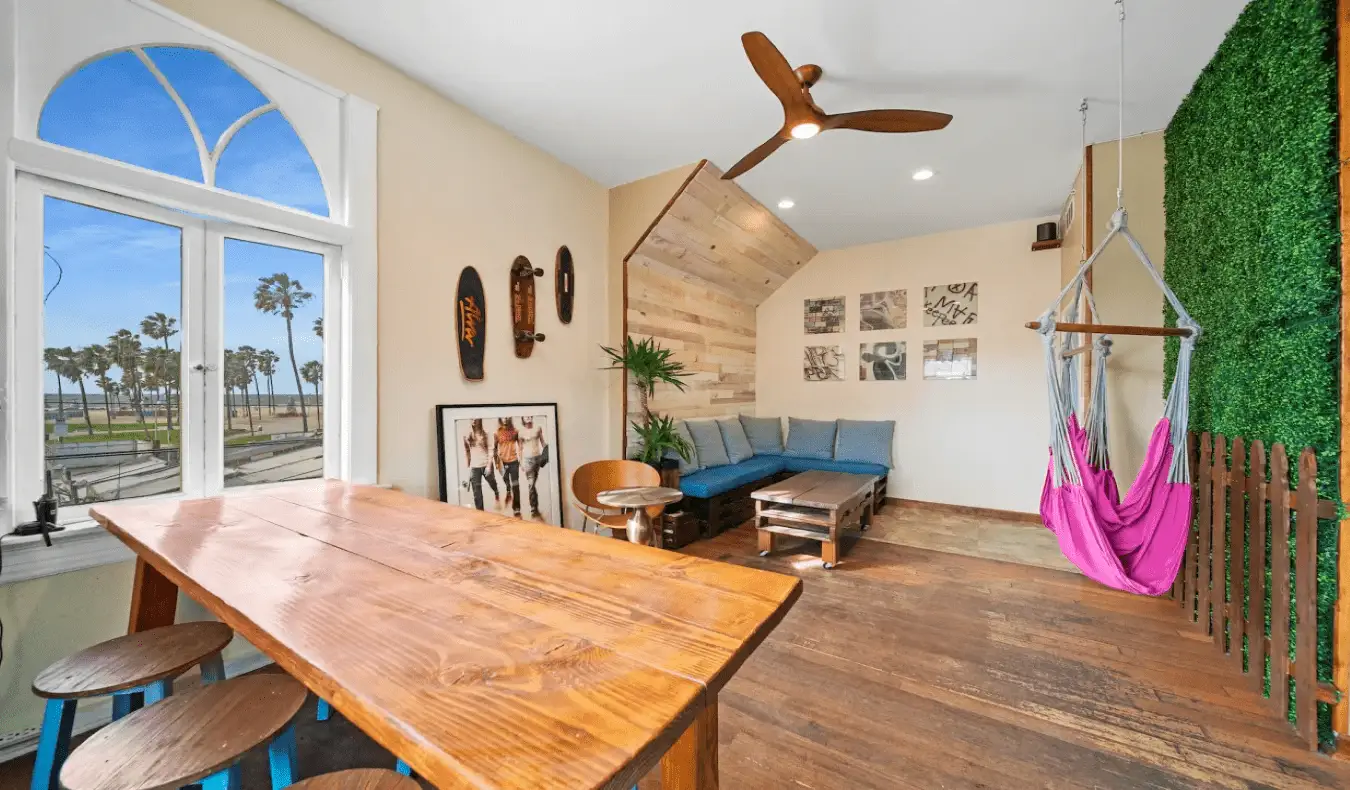 Sala común con una larga mesa de madera, hamacas y sofás en Samesun Venice Beach en Los Ángeles.