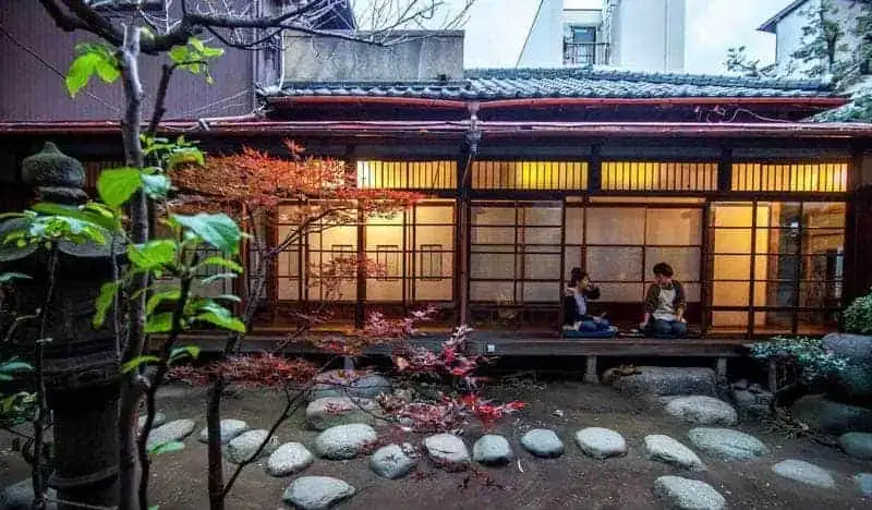 Cour intérieure avec jardin japonais traditionnel et personnes assises à l'extérieur des portes moustiquaires en bois du Toco Tokyo Hostel