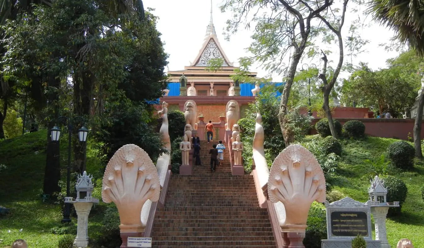 En høj trappe omgivet af træer og statuer, der fører op til Wat Phnom Daun Penh buddhisttempel i Phnom Penh