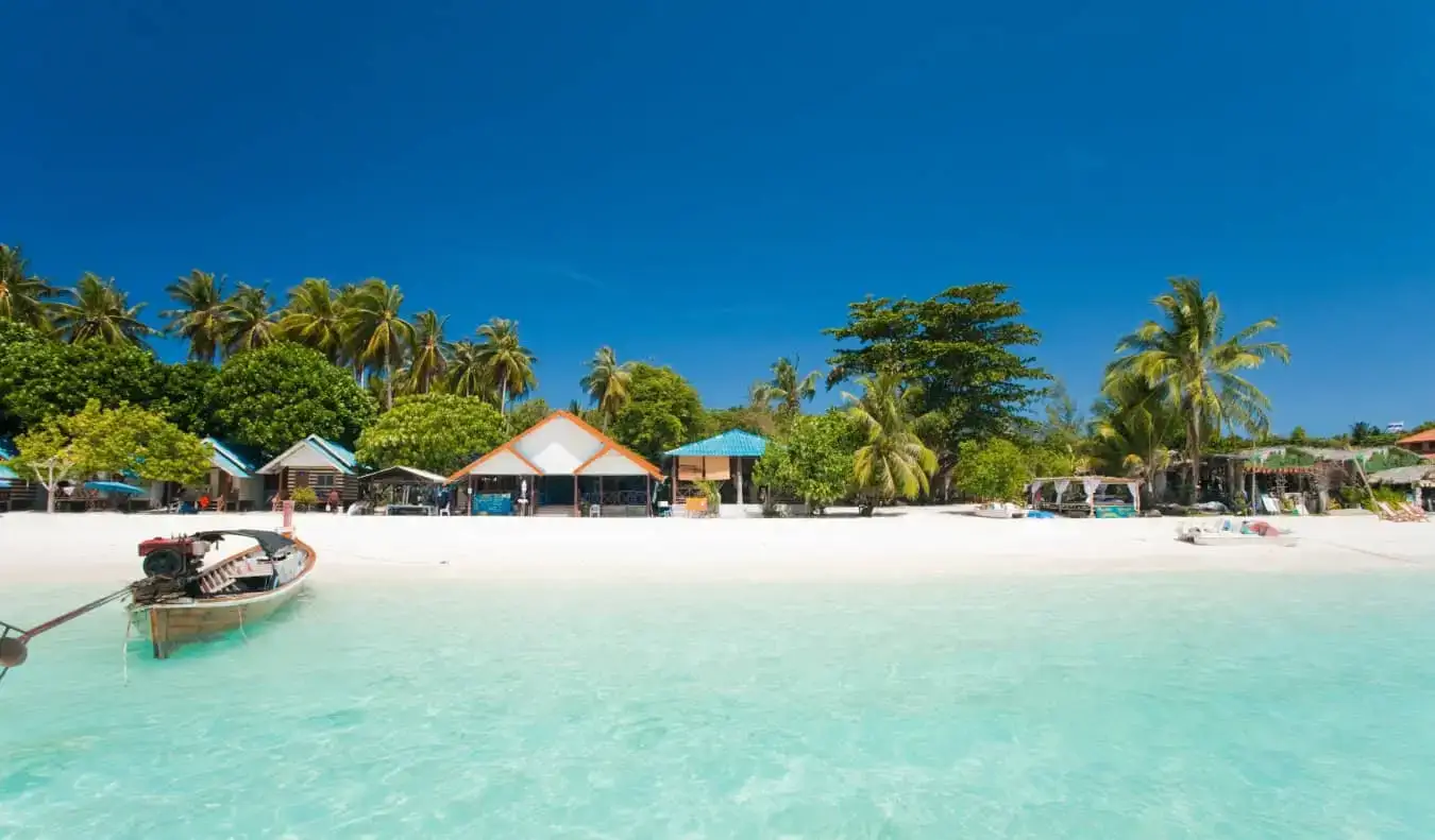 Bungalow lungo una spiaggia di sabbia bianca con una barca che galleggia di lato sull'isola di Ko Lipe in Thailandia