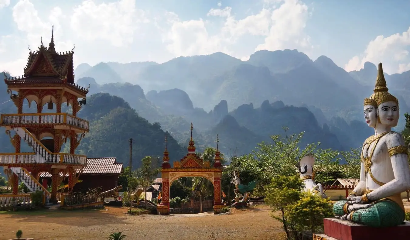 Patung Buddha, pagoda, dan gerbang merah menghadap pegunungan di Vang Vieng, Laos