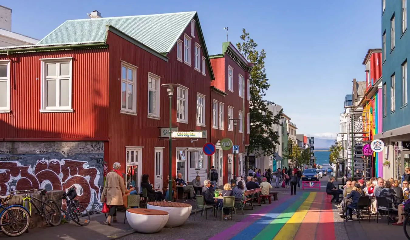 Een straatbeeld in Reykjavik, IJsland, met mensen die in cafés langs de regenbooggeschilderde straat zitten