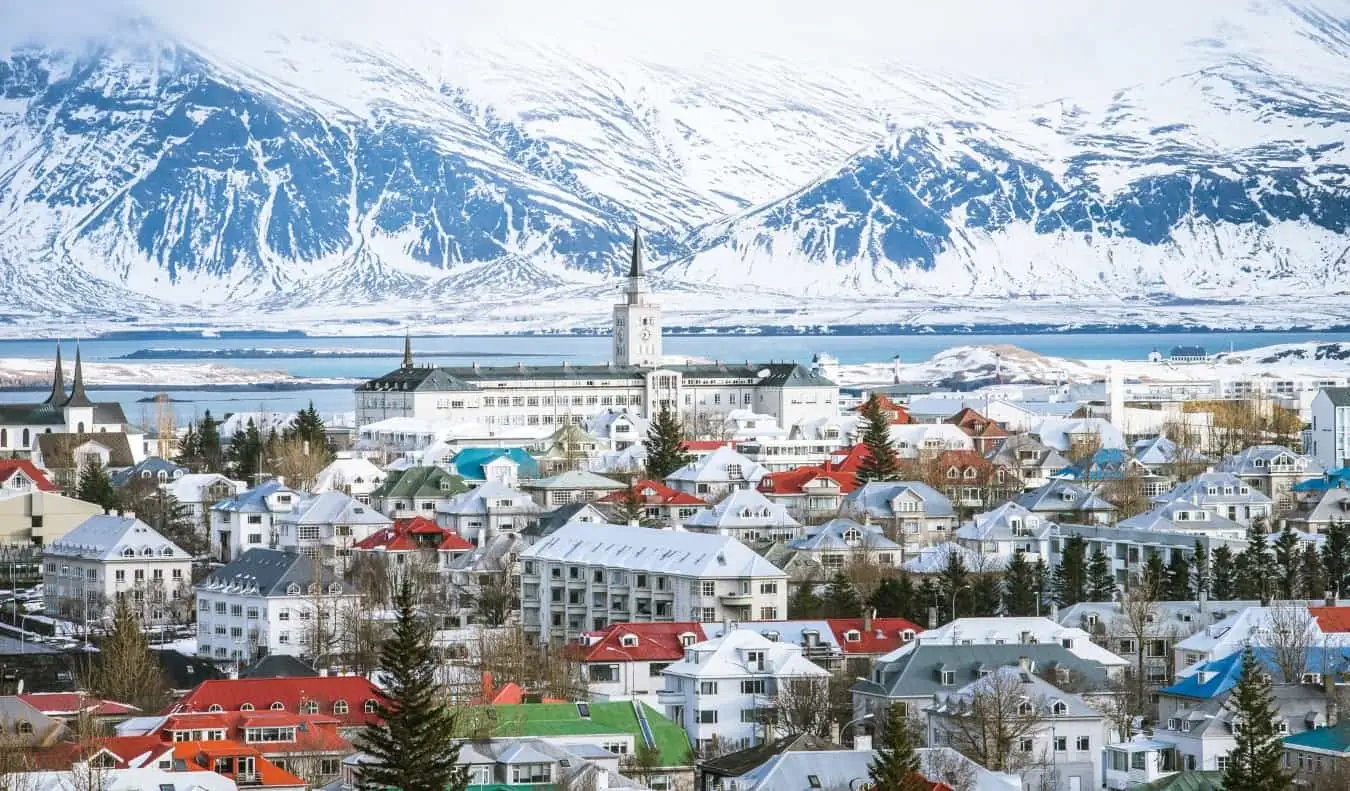 Reykjavík város látképe színes tetőkkel, templomtoronnyal és hóval borított hegyekkel a háttérben Izlandon