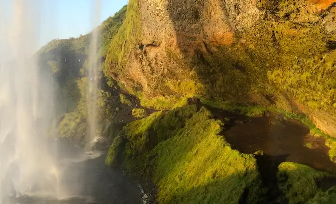 Parte trasera de Seljalandsfoss con excelente luz, agua, cielo azul y vegetación.