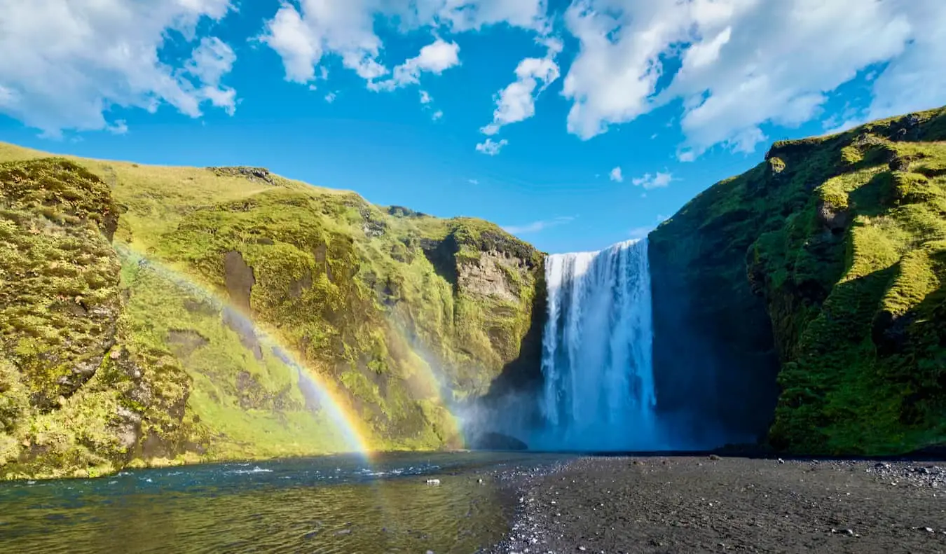 Augstais Skogafoss ūdenskritums saulainā Islandes laukos