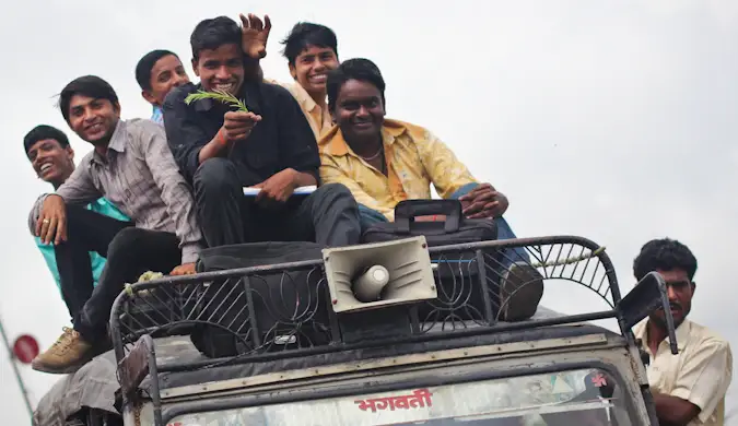 Een groep lokale bewoners bovenop een auto terwijl deze rijdt