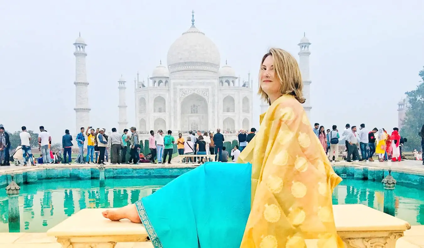 Seorang pelancong wanita solo dengan sari berwarna-warni berpose di depan Taj Mahal di India