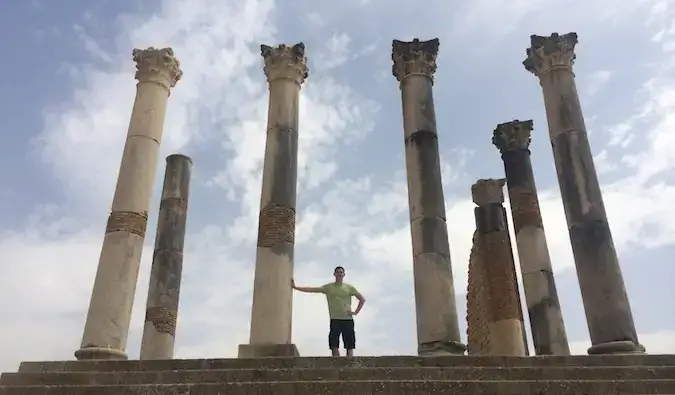 Nomadic Matt posing habang tinatangkilik ang Roman ruins ng Volubilis sa Morocco