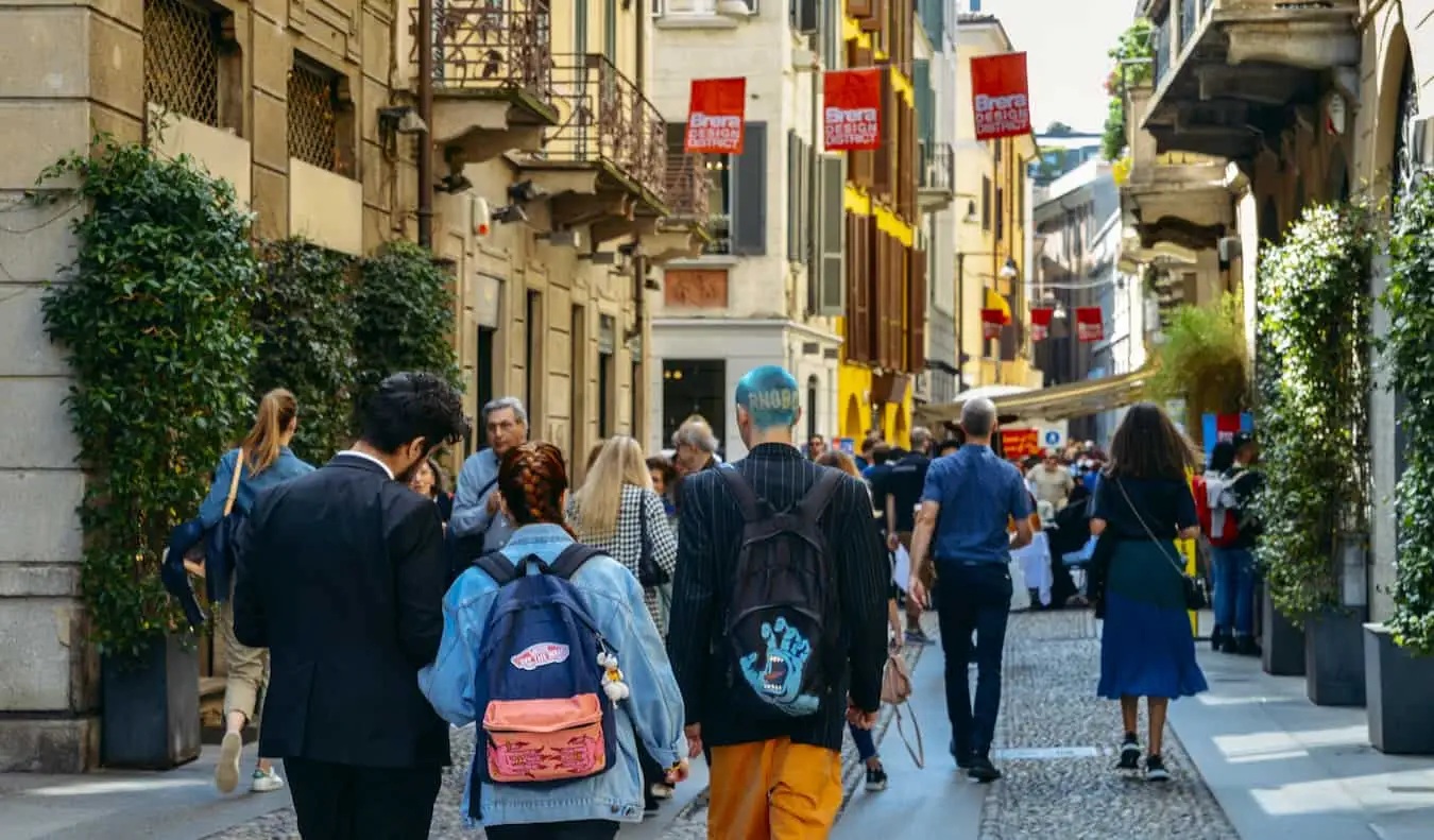 Persone che camminano su una strada stretta fiancheggiata da negozi e caffetterie nella vivace Milano, Italia