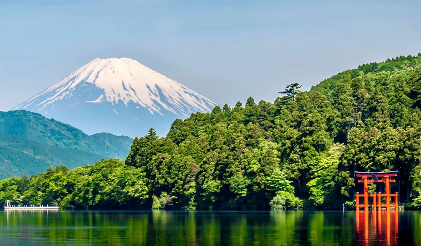 Een rode toriipoort in het water met weelderig groen en de berg Fuji op de achtergrond Japan