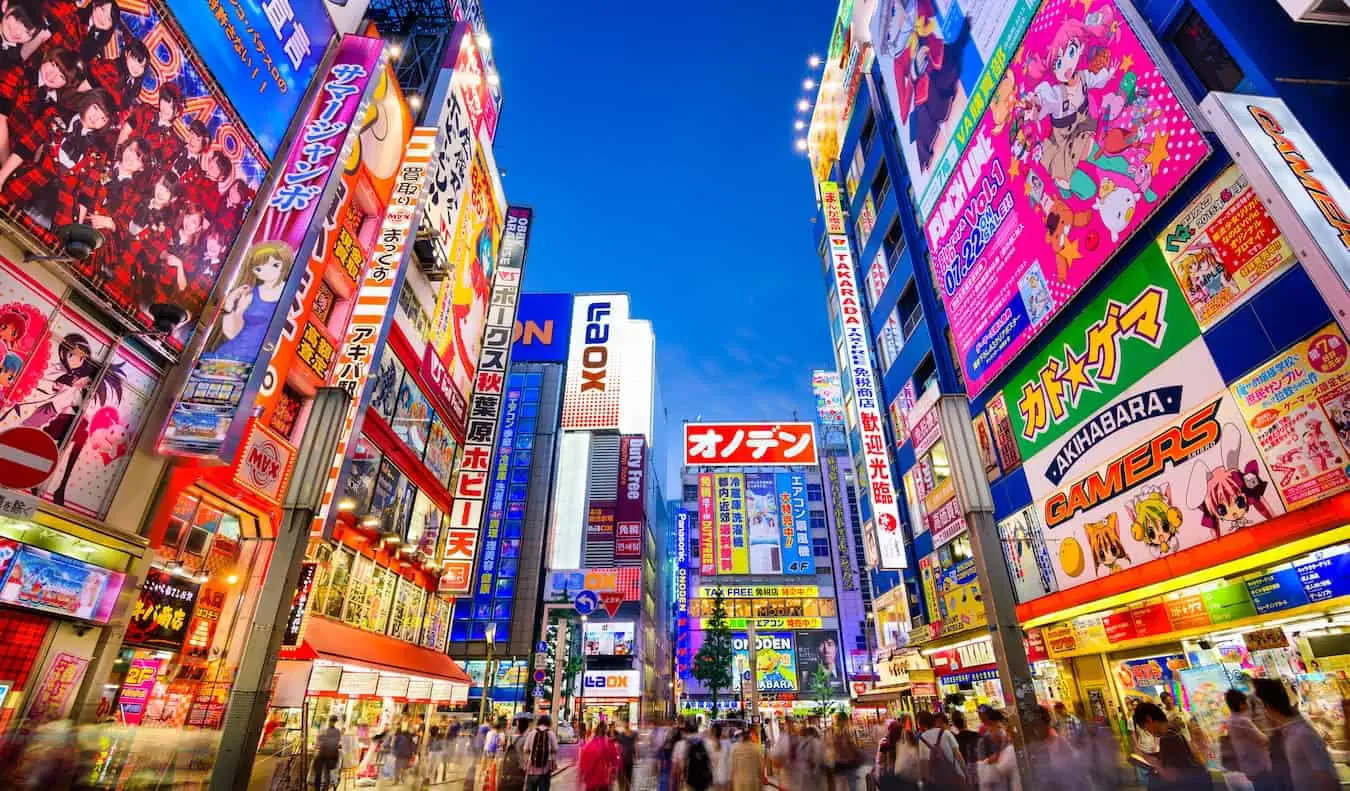 En lys og travl gade oplyst om natten med neonskilte i Tokyo, Japan