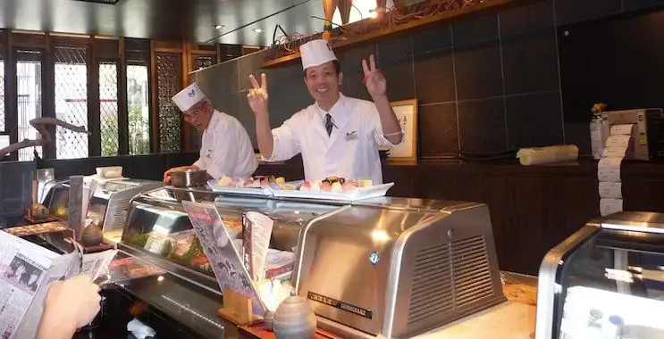 Japonský kuchař sushi pózuje pro přátelskou fotku zpoza pultu