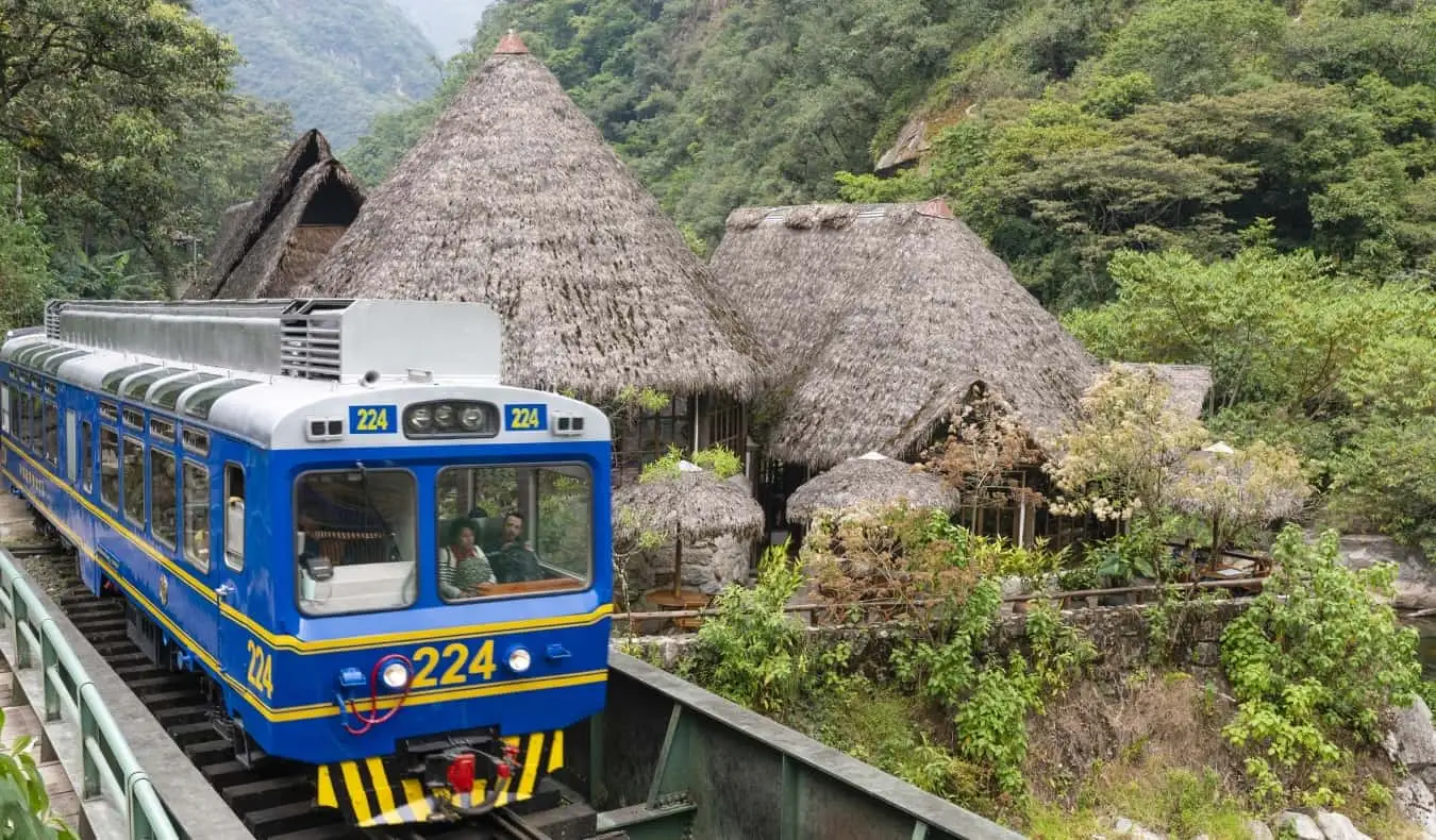 Stary niebieski pociąg przejeżdża obok domów krytych strzechą w pobliżu Machu Picchu w Peru