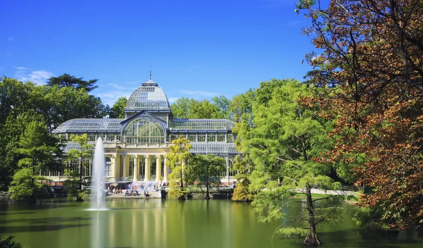 Madrid, İspanya'daki El Retiro Park'ta ağaçlarla çevrili küçük bir gölete bakan cam Kristal Saray