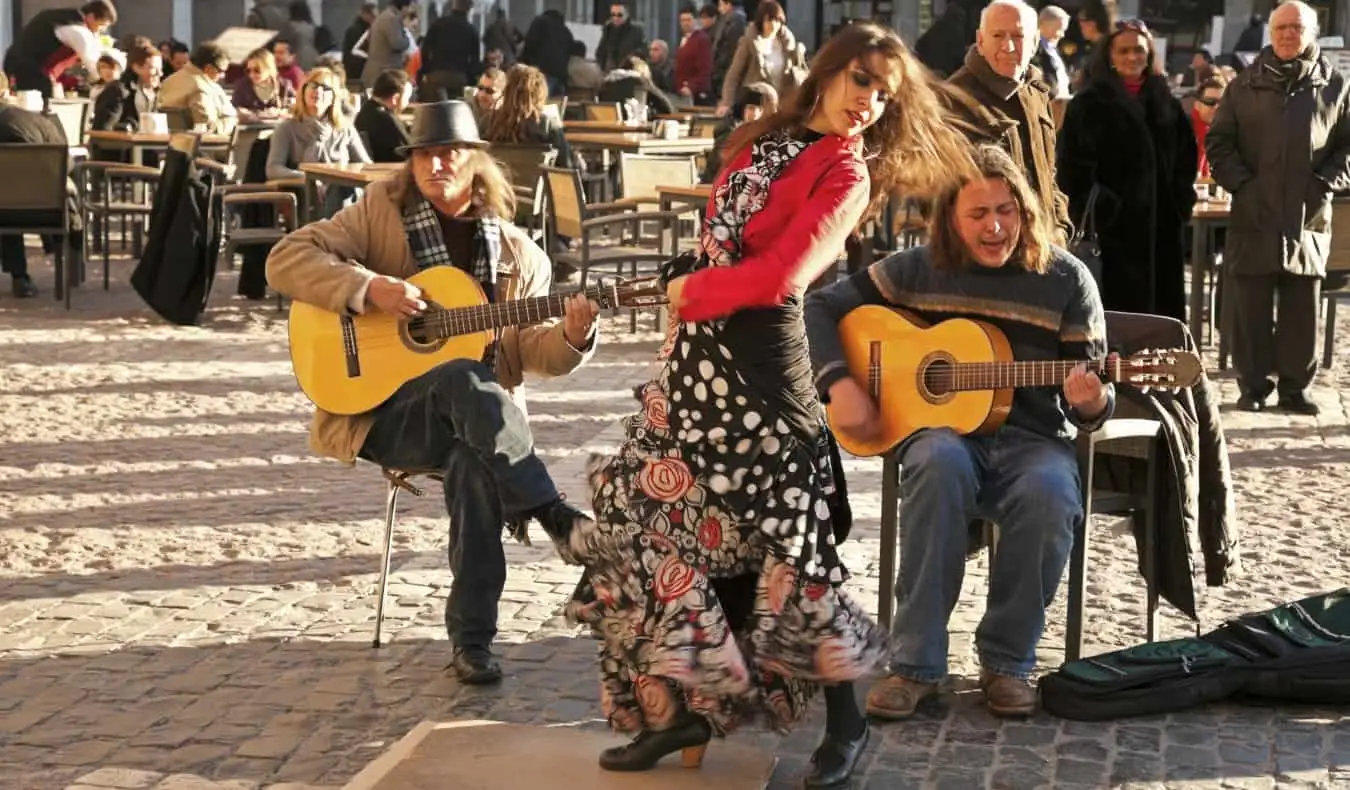 En kvinne danser flamenco akkompagnert av to gitarspillere bak seg på et torg i Madrid, Spania