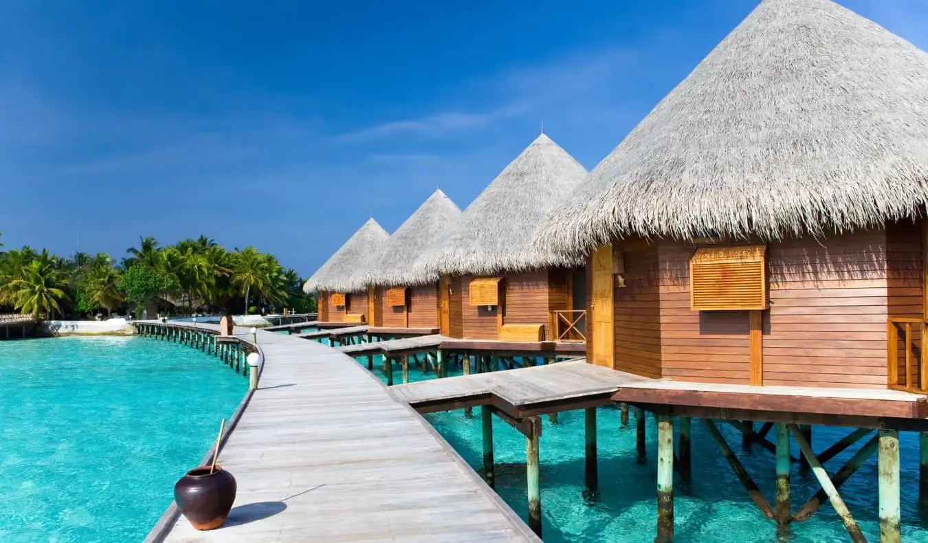 Huttes au toit de chaume menant à une promenade au-dessus des eaux cristallines des Maldives