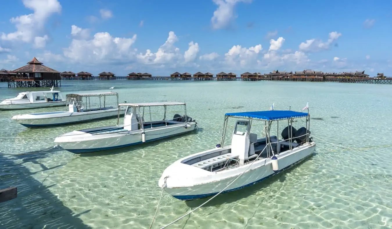 Boote legten mit strohgedeckten Bungalows über dem klaren Wasser im Hintergrund auf den Malediven an