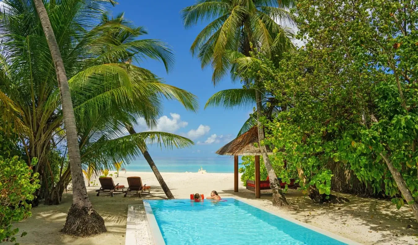 Mga taong nagrerelaks sa isang mahabang parihabang pool na napapalibutan ng mga palm tree at karagatan sa di kalayuan sa Maldives