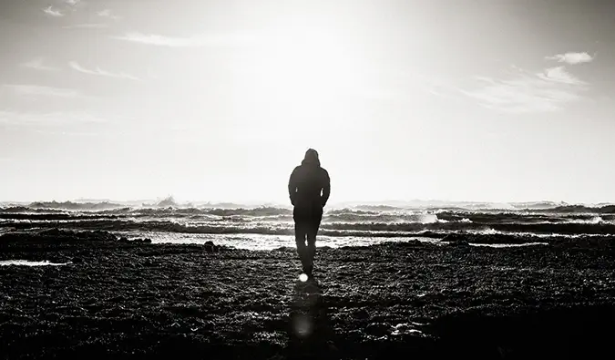 Una foto en blanc i negre d'un home caminant sol per una platja