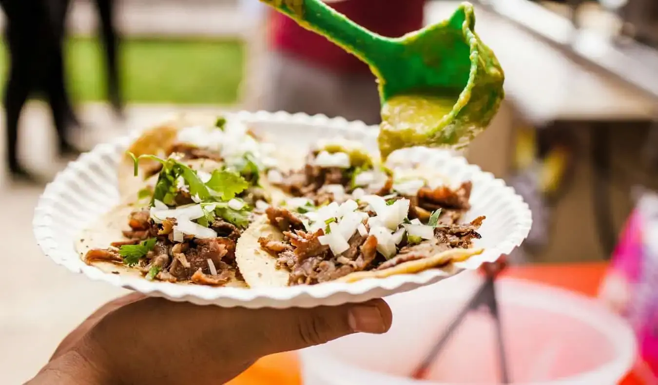 Isang kamay na may hawak na papel na plato na puno ng sariwang tacos sa Mexico City, Mexico