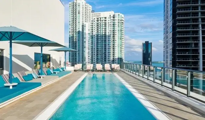 citizenM Miami Brickell 호텔의 플로리다주 마이애미의 고층 빌딩으로 둘러싸인 풀사이드 라운저가 있는 긴 직사각형 옥상 수영장