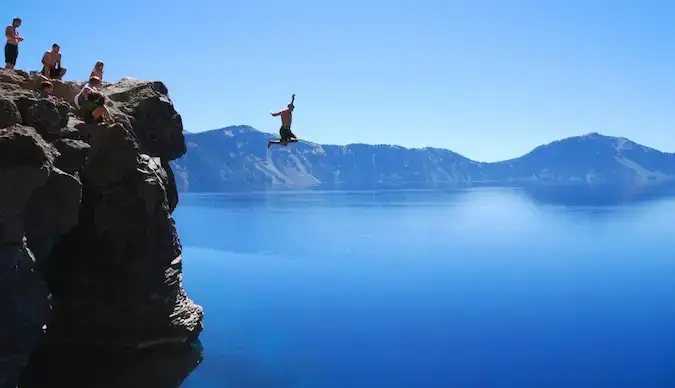 Un voyageur aventureux sautant par-dessus une falaise dans une eau bleue invitante