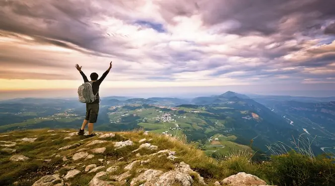 Seorang penjelajah solo yang mendaki, berdiri di puncak gunung