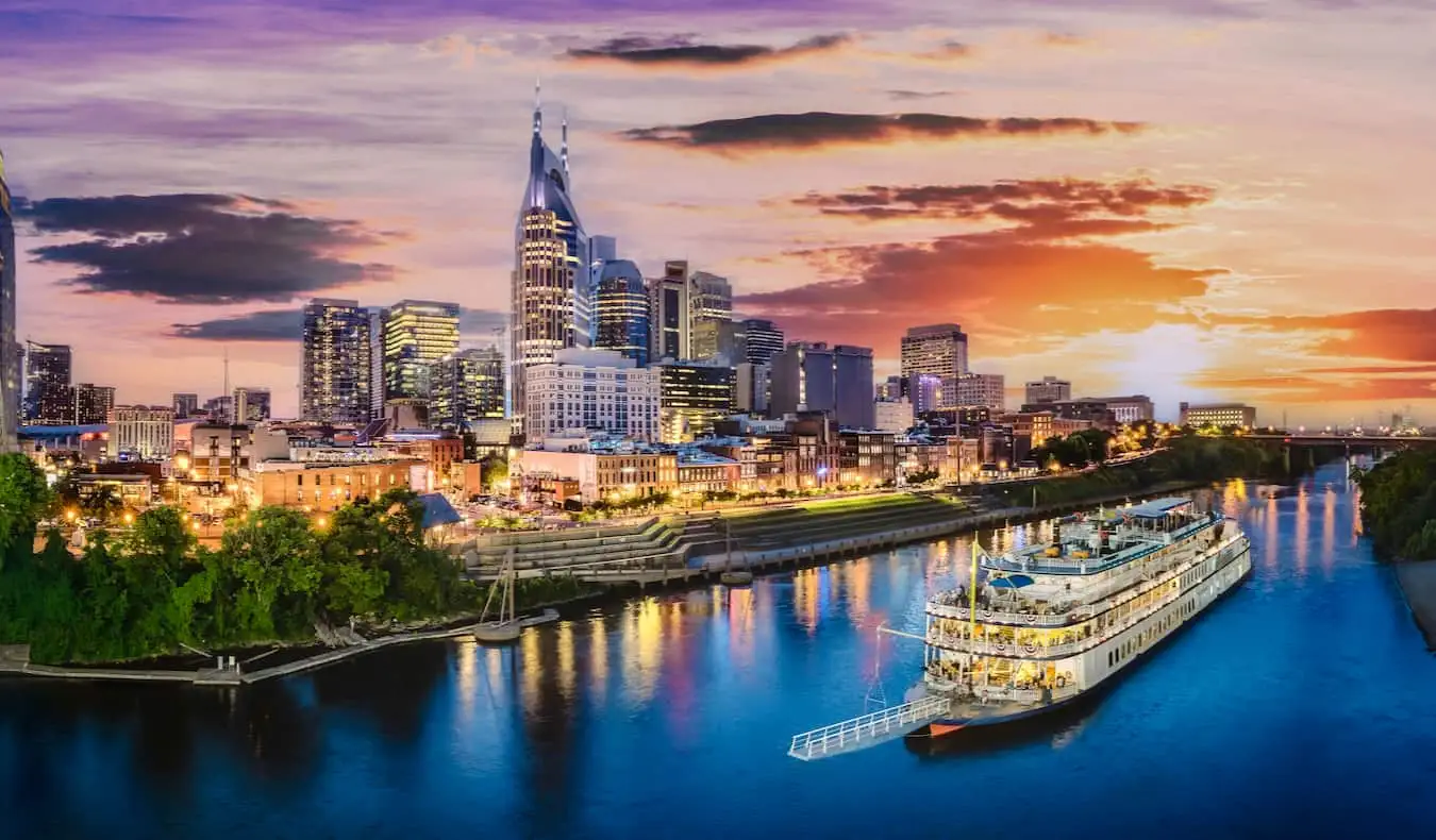 Die Skyline von Nashville, TN in der Abenddämmerung mit einem alten Boot, das in der Nähe auf dem Fluss fährt