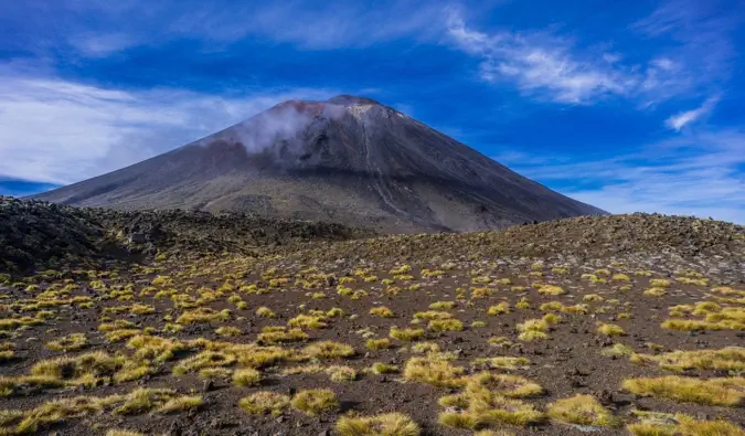 Un cer albastru deasupra versanților întunecați și abrupti ai Muntelui Ngauruhoe din traversarea alpină Tongariro din Noua Zeelandă