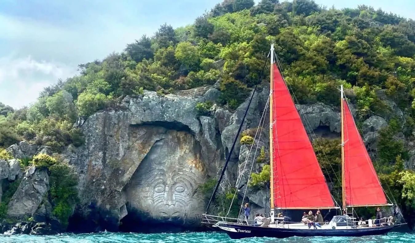 Perahu layar merah di hadapan ukiran batu Maori di Tasik Taupo di New Zealand