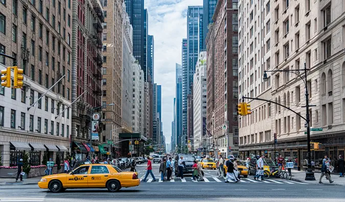 En livlig korsning med en gul hytt i New York City med massor av människor som korsar gatan