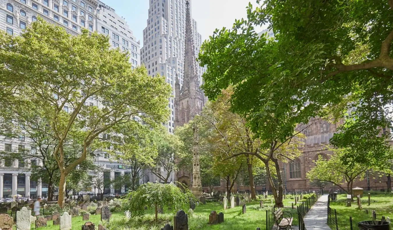 Gamle grave på en grøn kirkegård omgivet af træer ved Trinity Church i New York City, USA