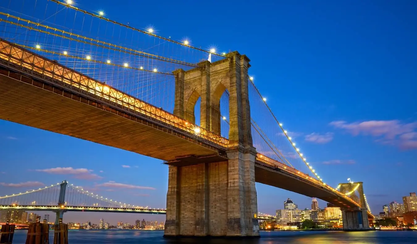 Toda a extensão da Ponte do Brooklyn em frente ao horizonte de Manhattan iluminada à noite na cidade de Nova York, EUA.