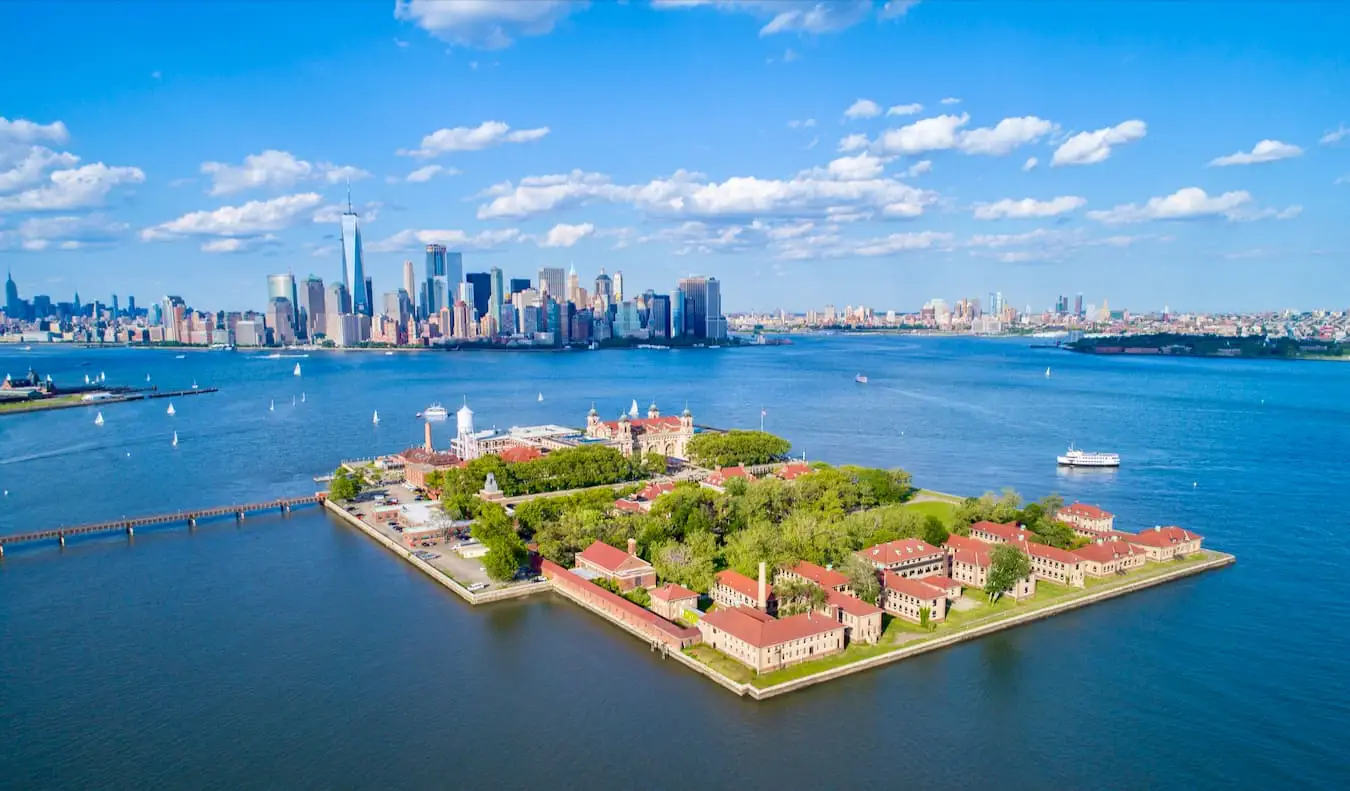 Het beroemde Ellis Island van bovenaf gezien met NYC op de achtergrond op een zonnige dag met blauwe lucht