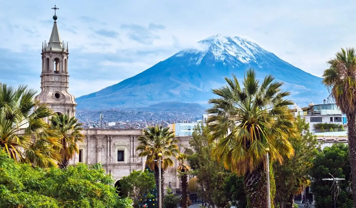 Horizonte de Arequipa, no Peru, com uma igreja histórica e palmeiras em primeiro plano e um vulcão ao fundo