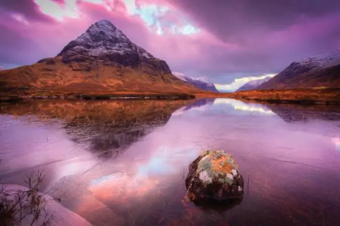 Betagende solnedgangsfoto over en frossen sø i Glencoe, Skotland