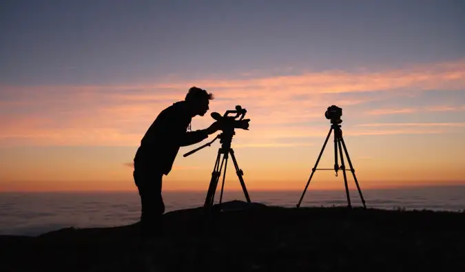 Un uomo che scatta foto su una montagna con due grandi fotocamere all'alba