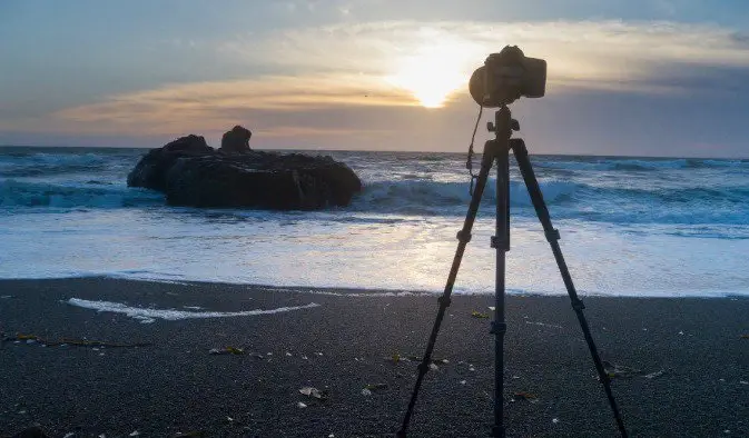 Statief en camera opgesteld op een natuurlijk strand in het buitenland tijdens een ontspannende zonsondergang