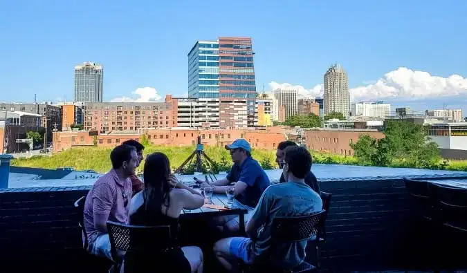 Un groupe de personnes sont assises à une table au Wye Hill Kitchen & Brewing avec l'horizon de Raleigh, en Caroline du Nord, en arrière-plan