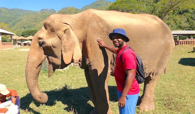 Alex stă lângă un elefant salvat în timp ce călătorește în Asia de Sud-Est