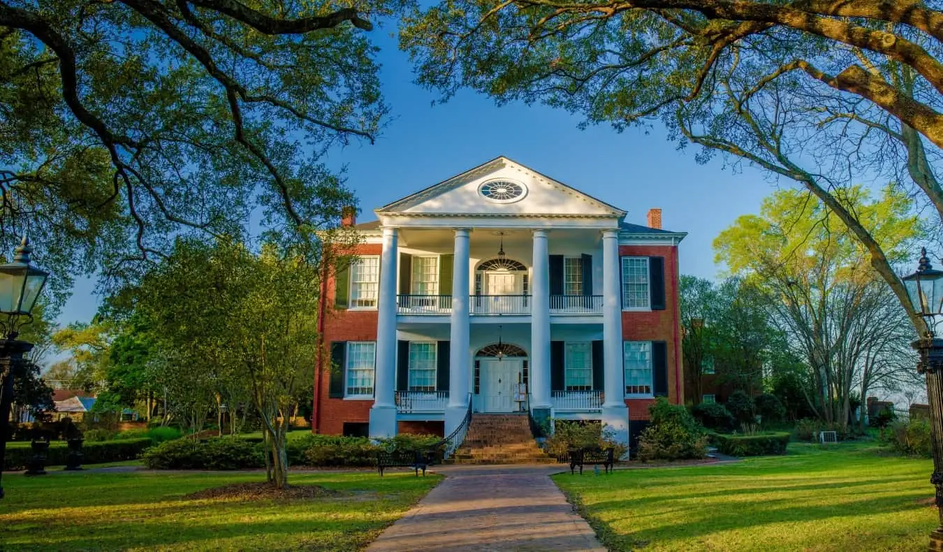 En sti som fører opp til det historiske herskapshuset Rosalie, med hvite søyler og en mursteinsfasade med svarte treskodder, omgitt av frodige trær i Natchez, Mississippi, USA