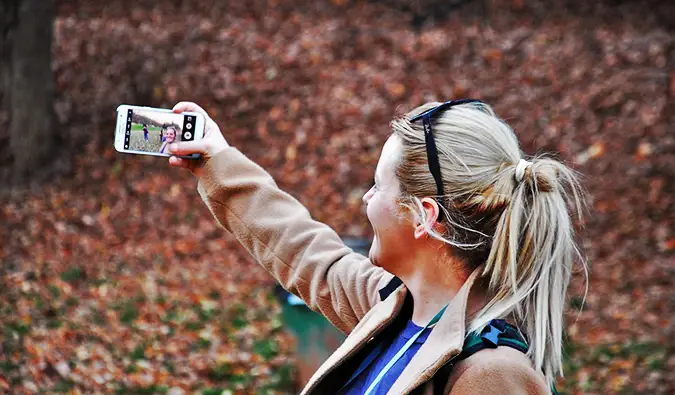 En kvinnelig alenereisende tar en selfie i skogen på en solrik dag