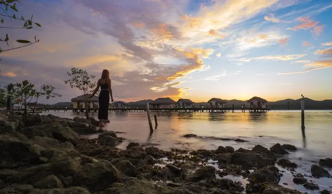 Une voyageuse seule devant un incroyable lever de soleil près de bungalows sur pilotis en Asie