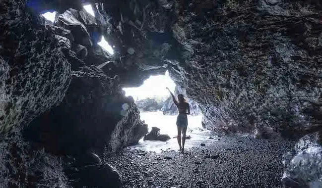 Pelancong wanita solo berpose untuk foto di sebuah gua dekat laut