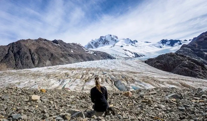 Uma viajante solitária sentada perto de montanhas cobertas de neve