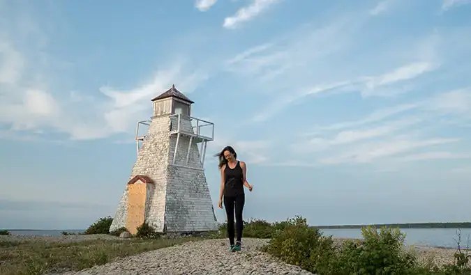 Naglalakad si Kirstin patungo sa camera na may lighthouse sa background